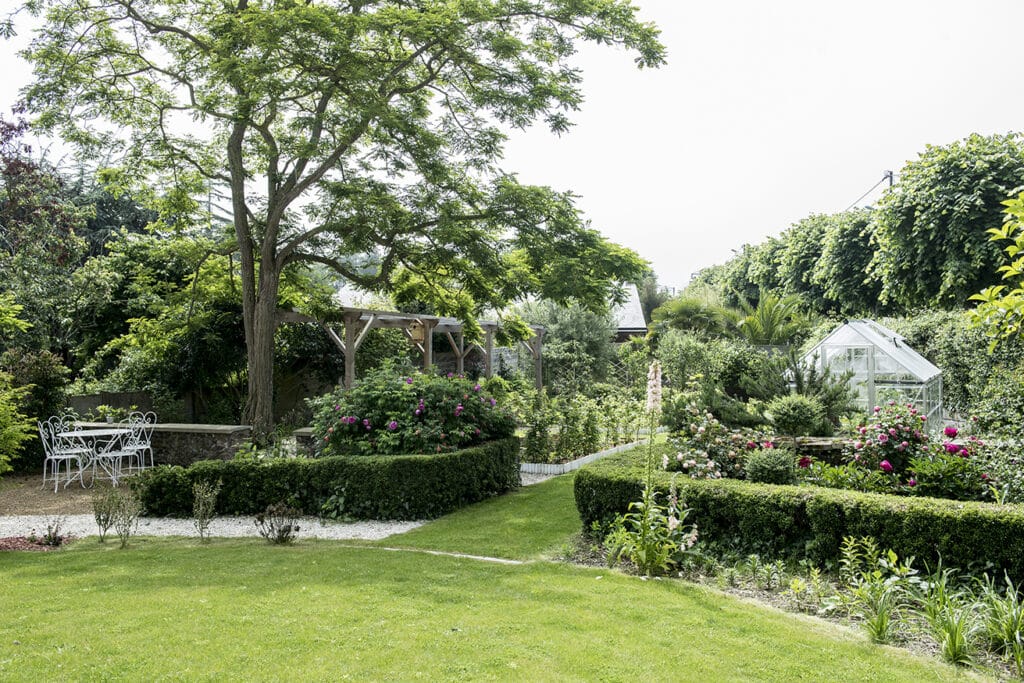 jardin verdoyant avec une serre, une table de jardin et des chaises